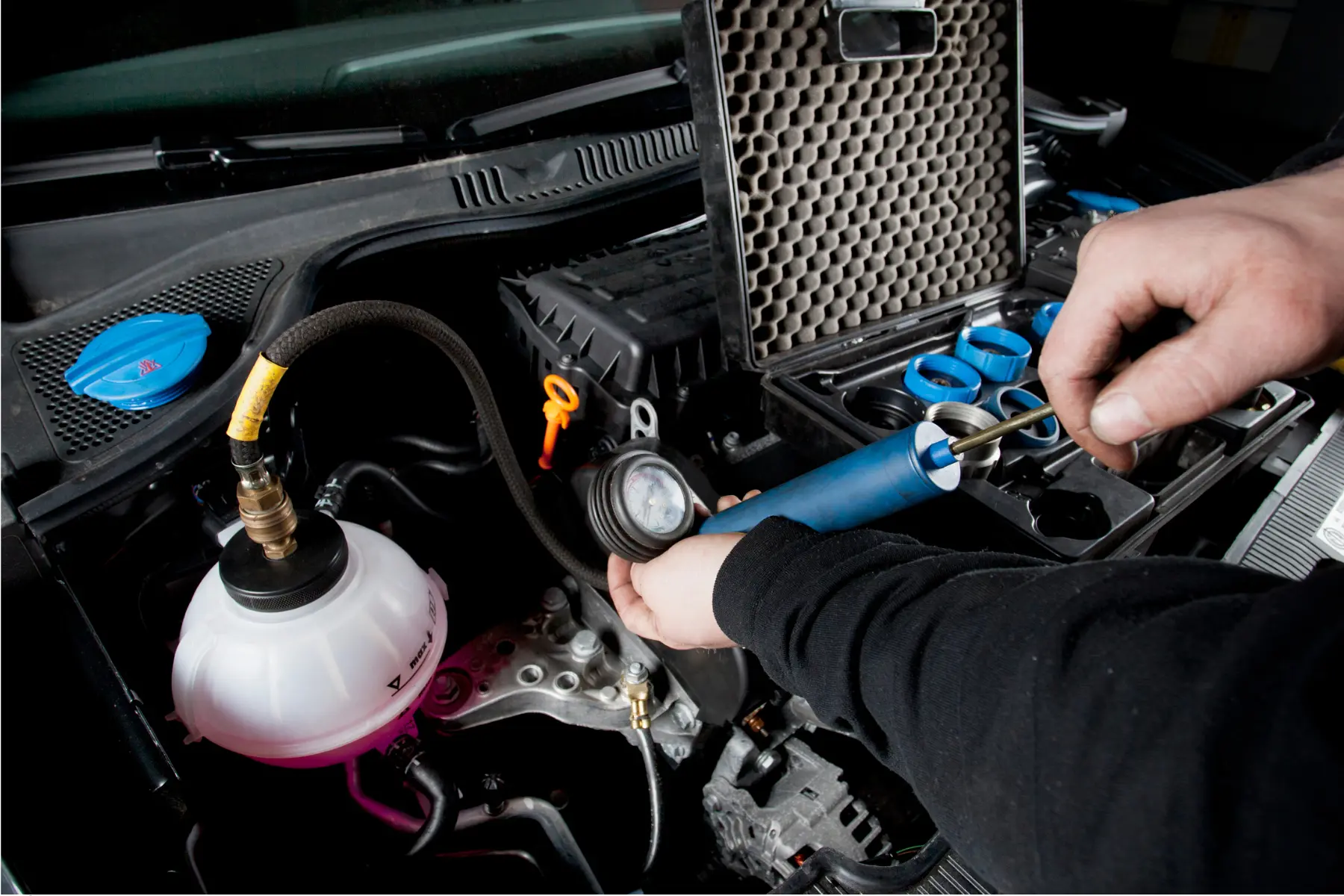 Mechanic checking or flushing a car’s cooling system using a specialized tool.