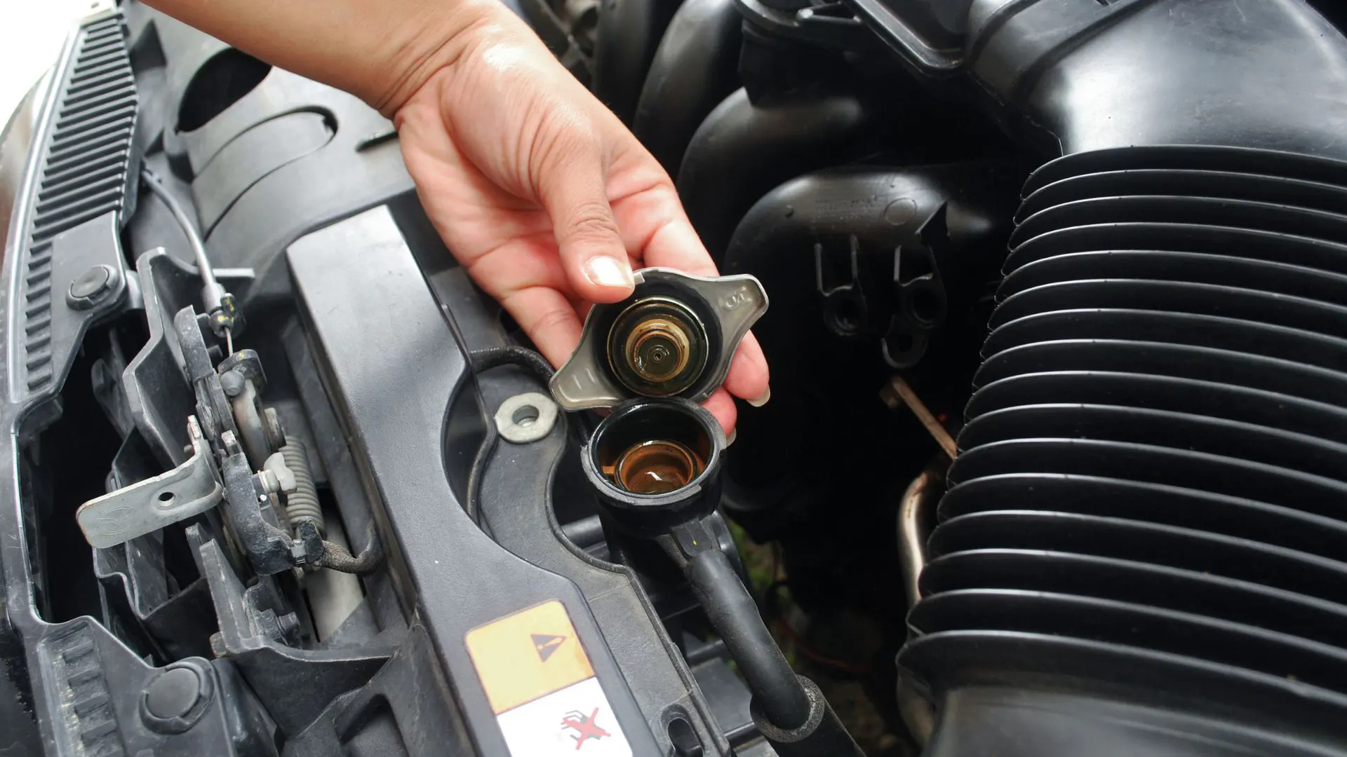 Hand holding a radiator cap over the radiator opening in a car.