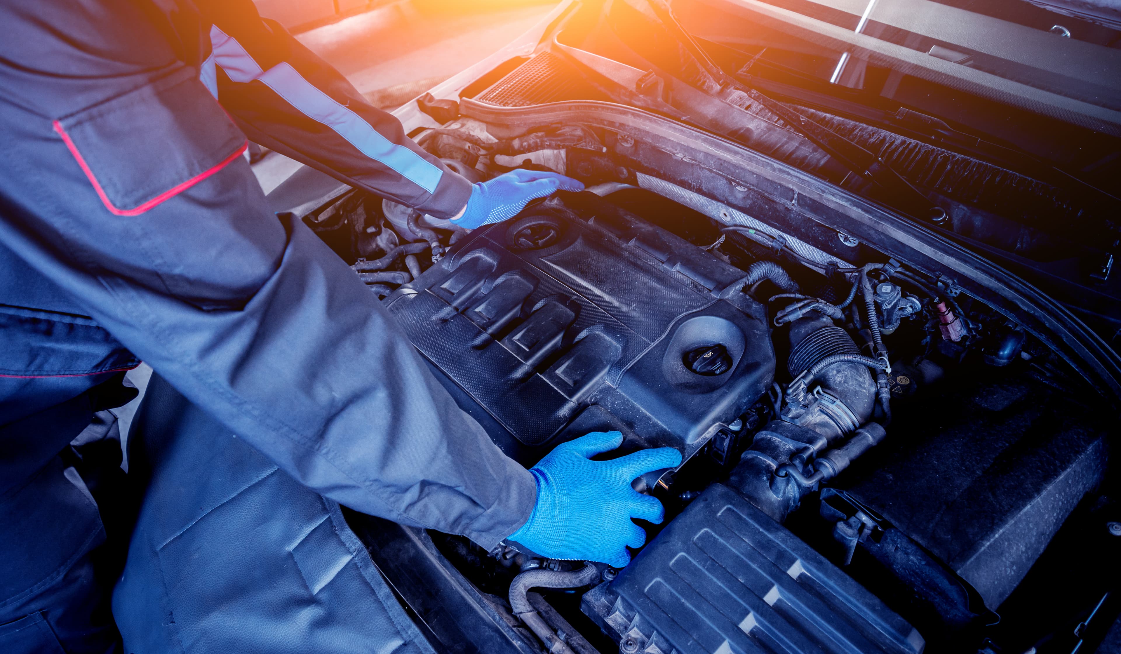 Mechanik w rękawicach ochronnych sprawdza i naprawia silnik samochodu w świetle słonecznym