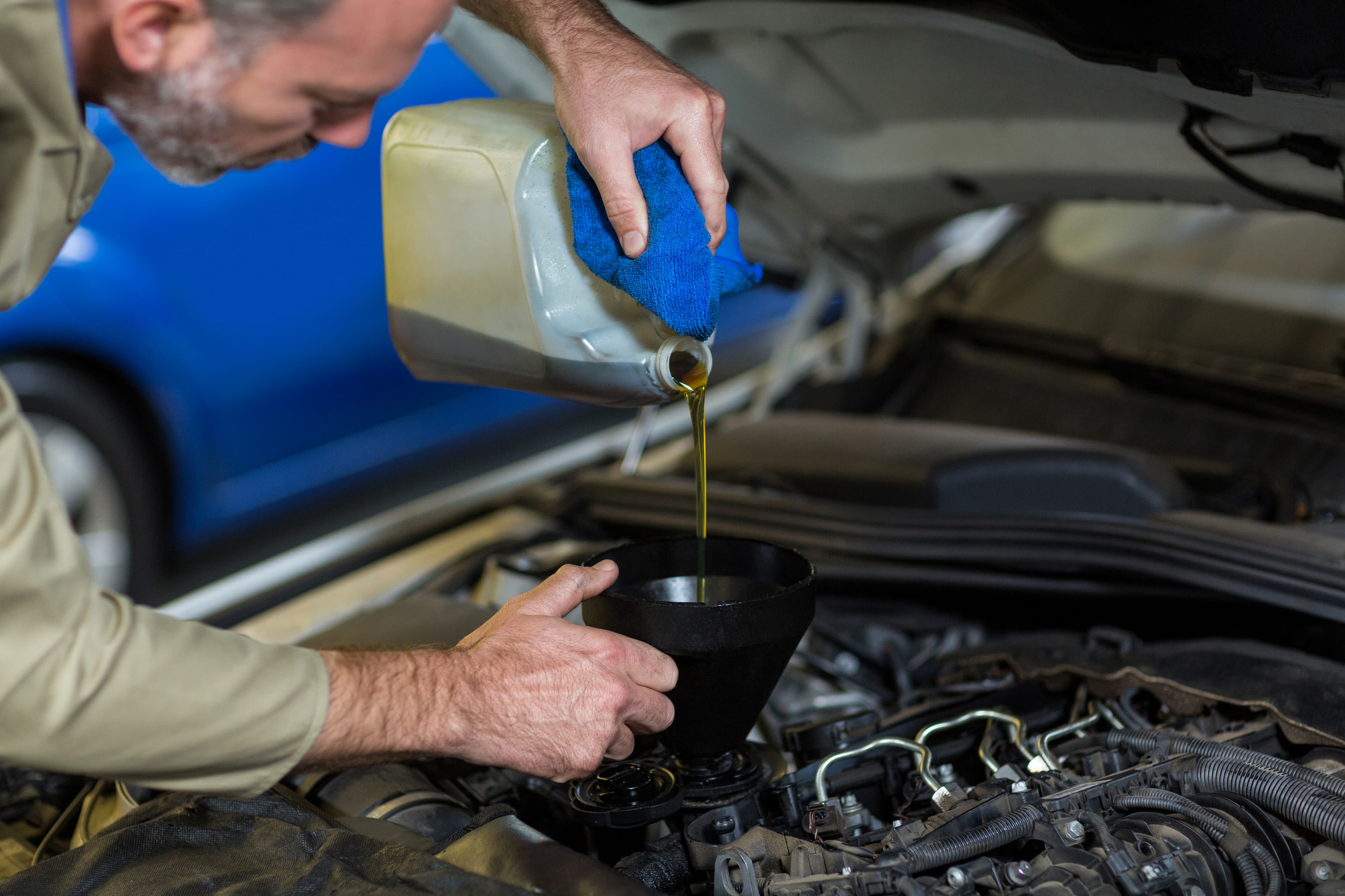 Person pouring fresh motor oil into the engine using a funnel